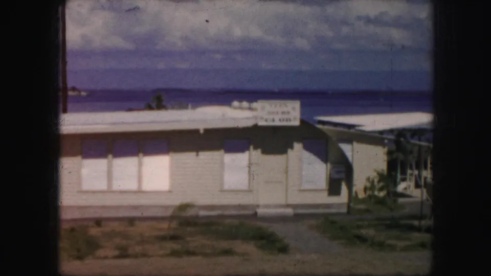 1959 Kansas City home-movie frame of a lakeside building with a readable Teen Club sign, shuttered windows, and lake beyond.