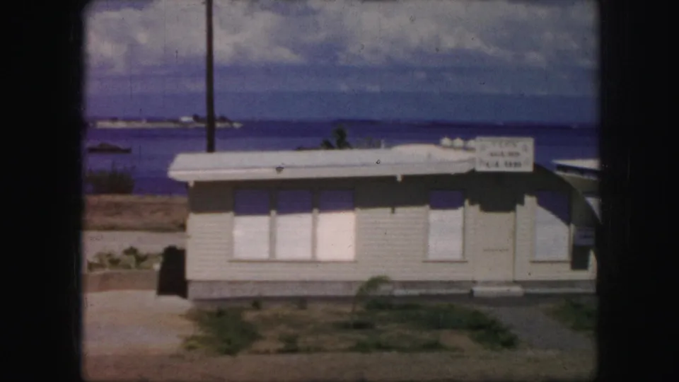 1959 Kansas City frame showing the Teen Club building beside a lake, with a road, utility pole, and distant shoreline visible.
