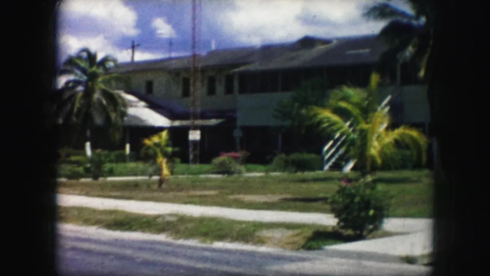 Soft 8mm frame of a raised residential building, palms, shrubs, lawn, sidewalk, and street curb, supported by 1959 Kansas City metadata.