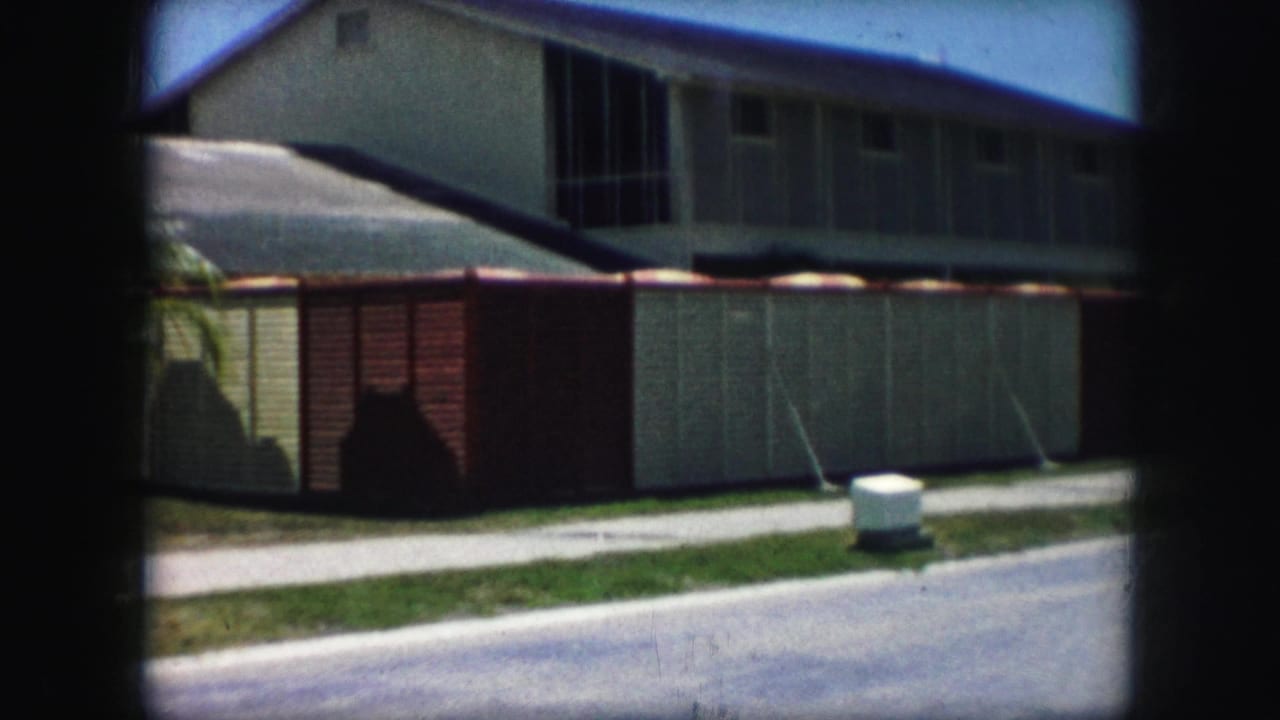 House exterior with sloped roof, block wall, sidewalk, grass, and street.