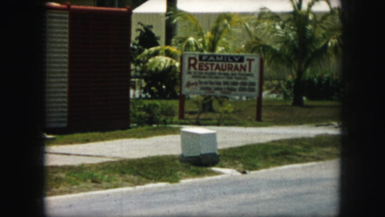 1959 Kansas City frame with a family restaurant sign, curb, grass, and palms seen through the divided 8mm contact-sheet frame.
