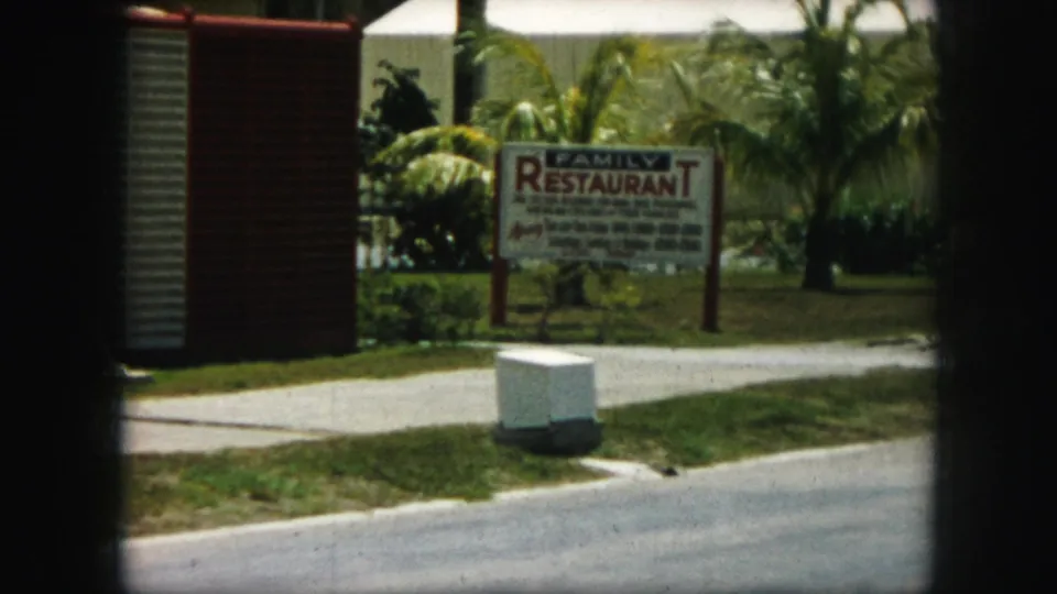 1959 Kansas City frame with a family restaurant sign, curb, grass, and palms seen through the divided 8mm contact-sheet frame.