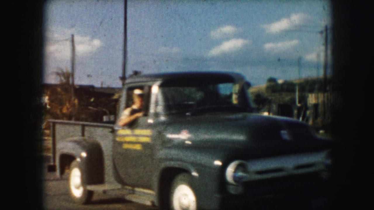 A dark green pickup truck passes through the 1959 Kansas City street scene, with a man visible in the driver's seat.