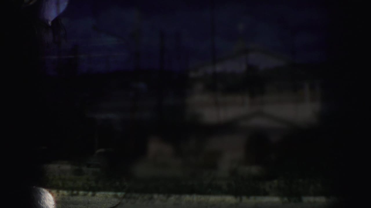 Dark partial film frame with a faint exterior building shape and heavy underexposure.