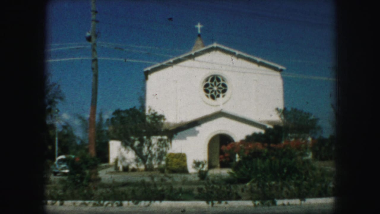 White church exterior in Kansas City, Missouri, 1959, showing a cross, circular stained-glass window, arched doorway, shrubs, and a parked car.
