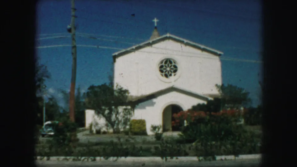 White church exterior in Kansas City, Missouri, 1959, showing a cross, circular stained-glass window, arched doorway, shrubs, and a parked car.