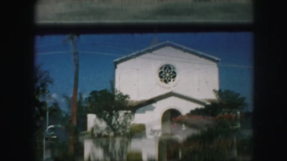 Softly focused 1959 Kansas City church exterior with a white facade, cross, circular window, arched doorway, shrubs, and dark frame edges.