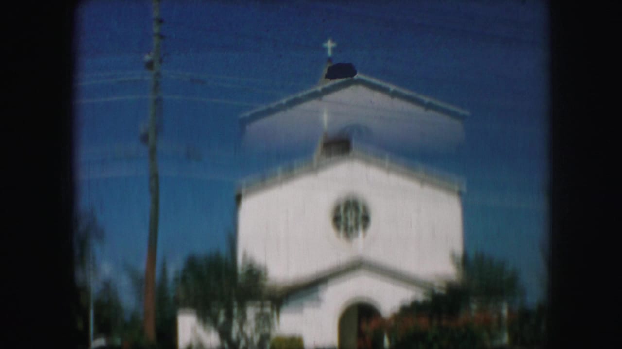 1959 Kansas City frame of a white church exterior with cross, circular rose window, utility pole, trees, and soft 8mm focus.