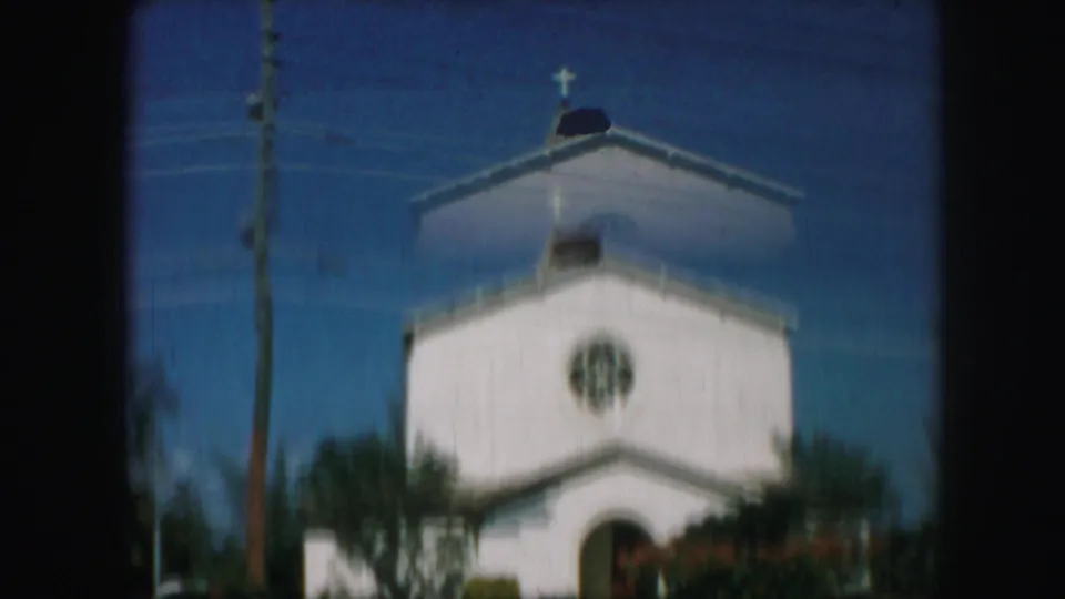 1959 Kansas City frame of a white church exterior with cross, circular rose window, utility pole, trees, and soft 8mm focus.