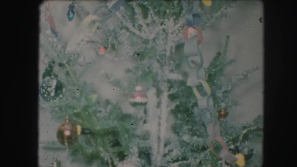 1959 Kansas City home-movie frame of a flocked Christmas tree with visible ornaments, paper chain, and colored light bulbs.