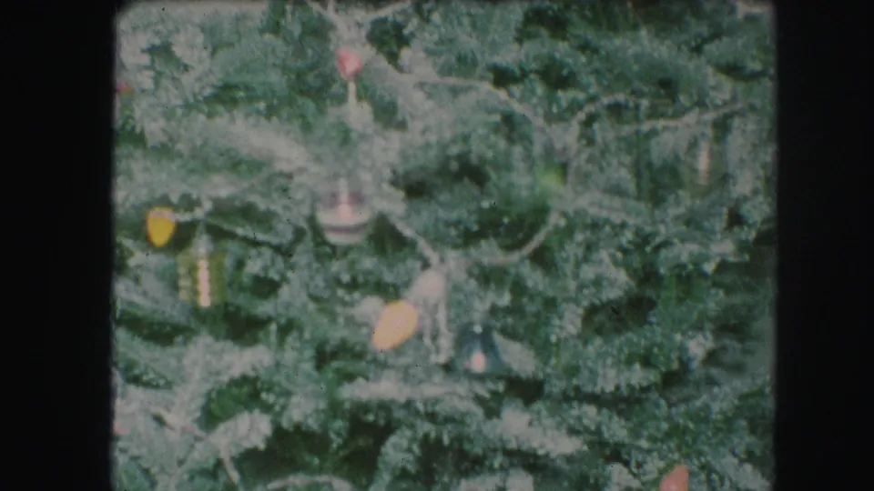 1959 Kansas City home-movie frame with a decorated Christmas tree and a blurred hand appearing to adjust an ornament or branch.