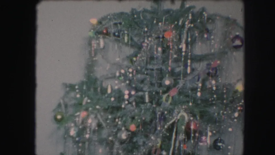 1959 Kansas City 8mm frame showing the upper section of a decorated green Christmas tree with tinsel, ornaments, and soft indoor light.