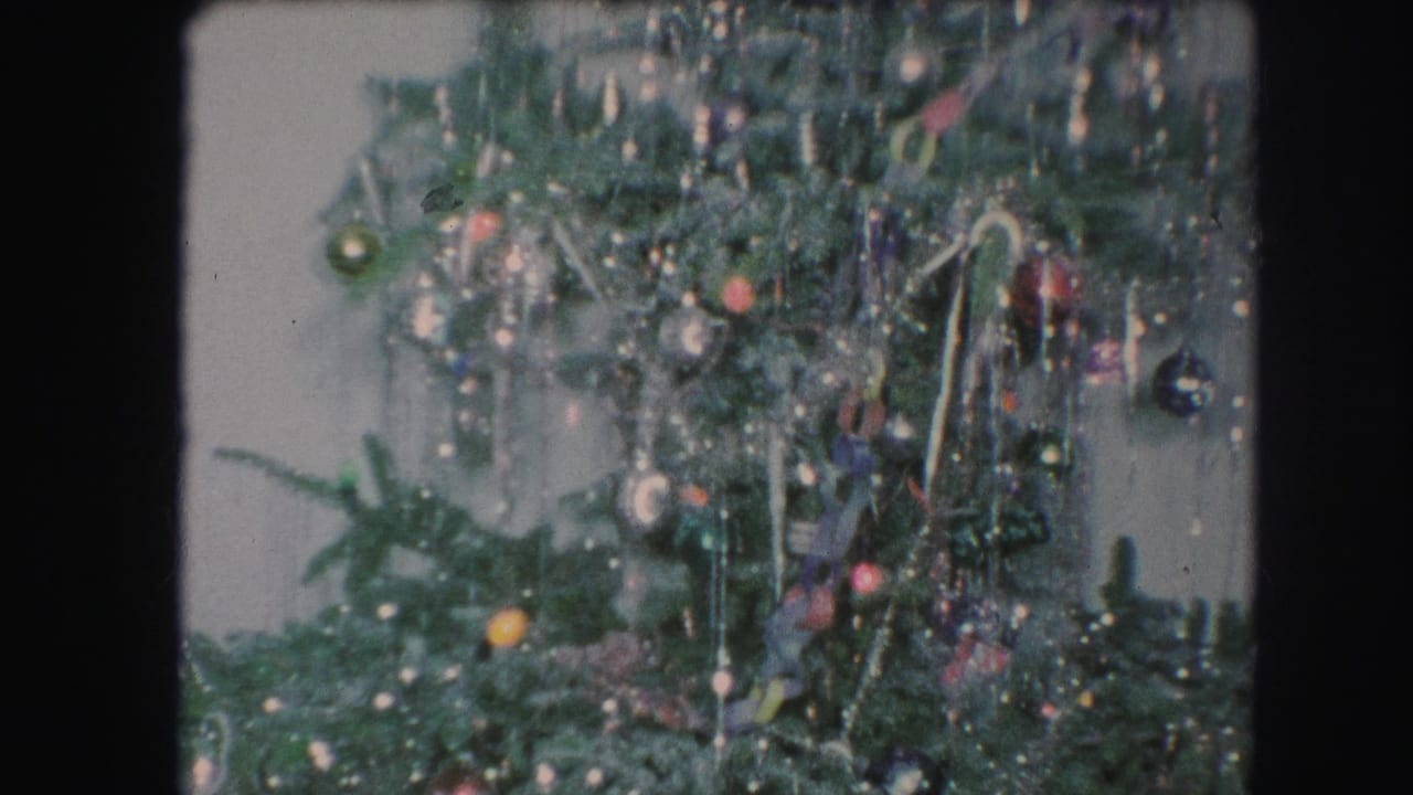 1959 Kansas City home-movie frame of a Christmas tree section dense with tinsel, colored ornaments, and small lights.