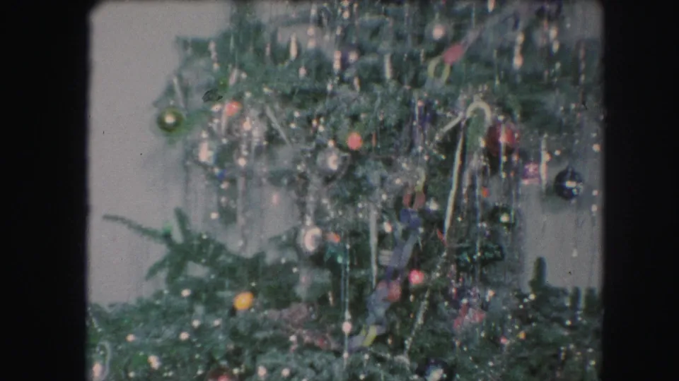 1959 Kansas City home-movie frame of a Christmas tree section dense with tinsel, colored ornaments, and small lights.