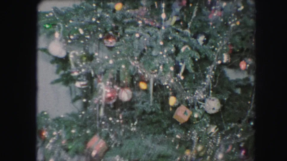 1959 Kansas City home-movie frame with a decorated green Christmas tree, silver tinsel, colorful ornaments, and soft 8mm texture.