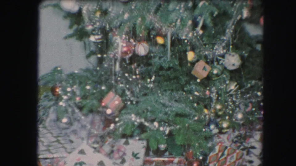 1959 Kansas City home-movie frame showing a decorated Christmas tree with tinsel, ornaments, lights, and gifts beneath it.