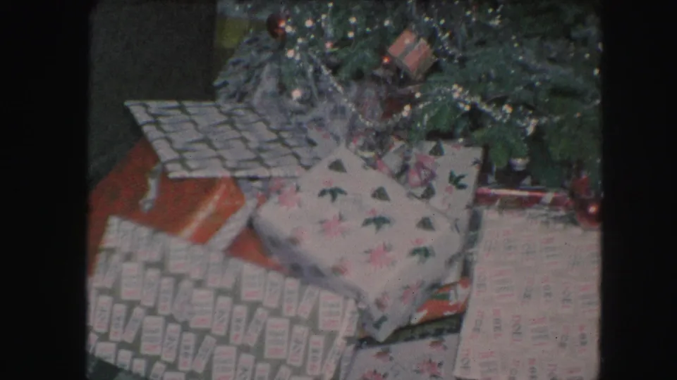 1959 home-movie view of presents beneath a decorated Christmas tree, with retro wrapping patterns and visible film grain.