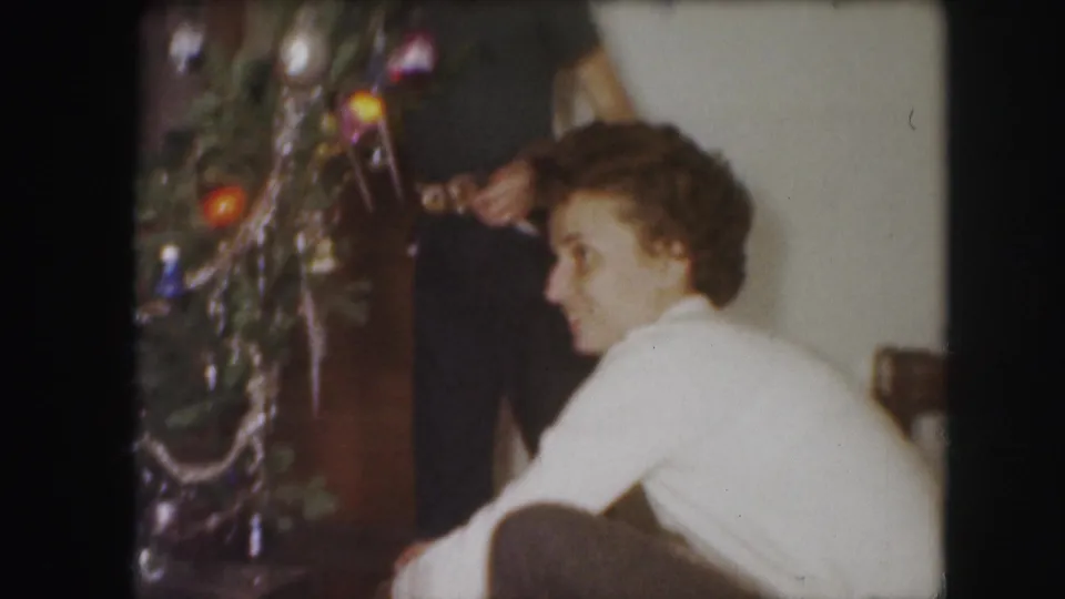 1959 Kansas City home-movie frame with a woman seated near a tinsel-covered Christmas tree in a living room.