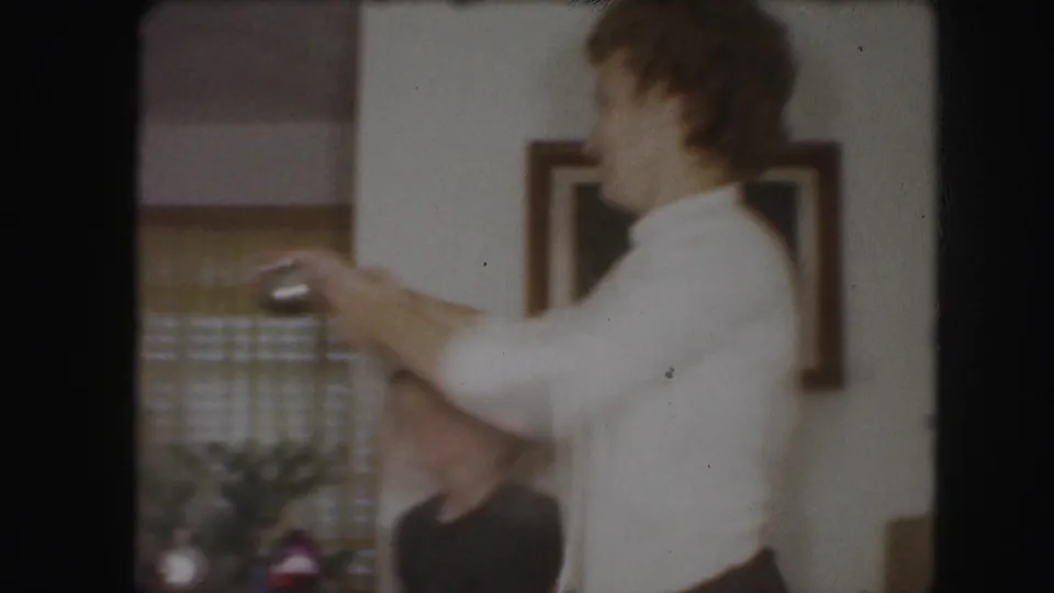 1959 Kansas City home-movie frame with a woman in profile handling a small object near holiday decorations indoors.