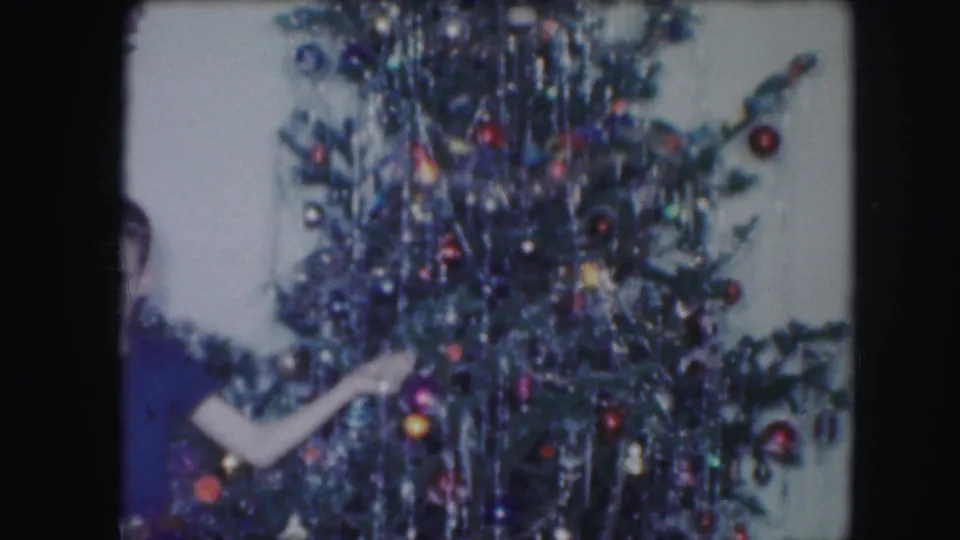 Lower view of the decorated tree as a partially visible person reaches in, matching the 1959 Kansas City home-movie context.