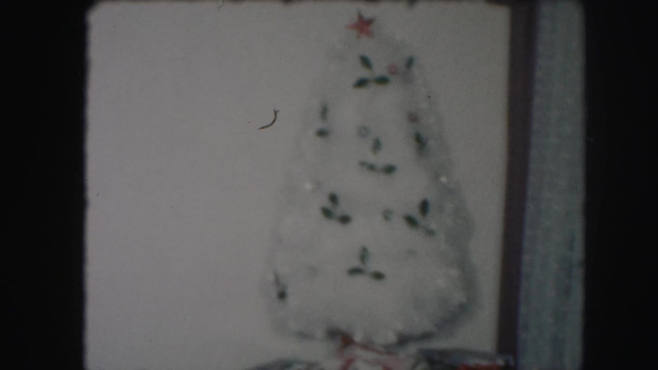White artificial Christmas tree with small ornaments against a wall.