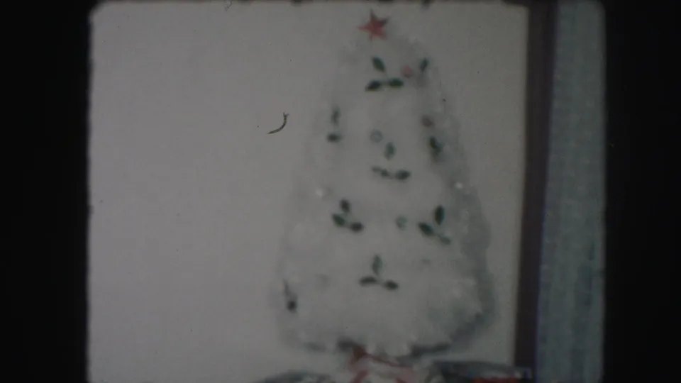 A 1959 8mm frame from Kansas City showing a white artificial Christmas tree with green ornaments and a red star topper.