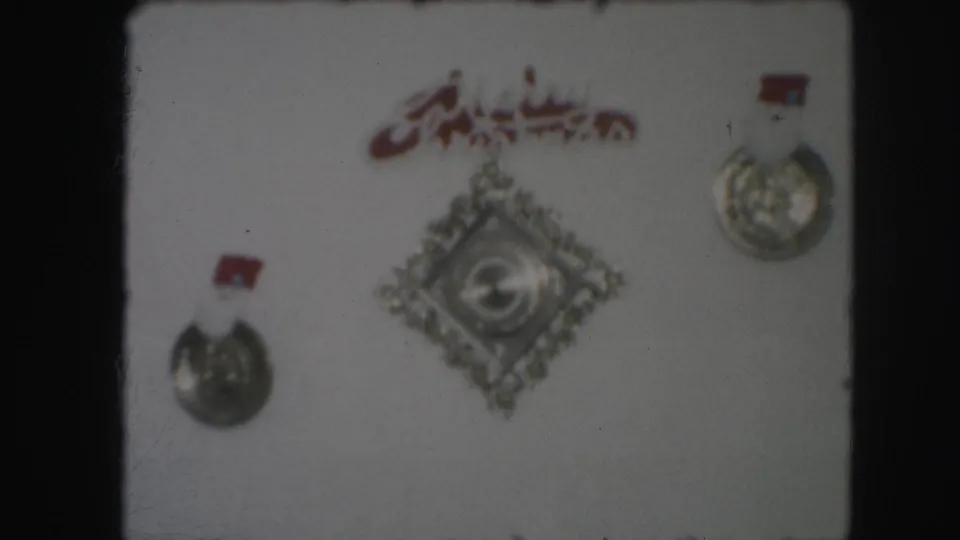 Soft 8mm view of a wall display with two silver medals, red tabs, red script, and a central diamond-shaped emblem.