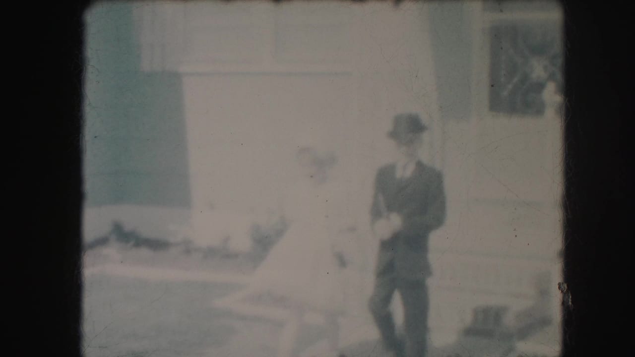 In 1959 Kansas City home-movie footage, a formally dressed boy stands near a girl in a white dress in a suburban yard.