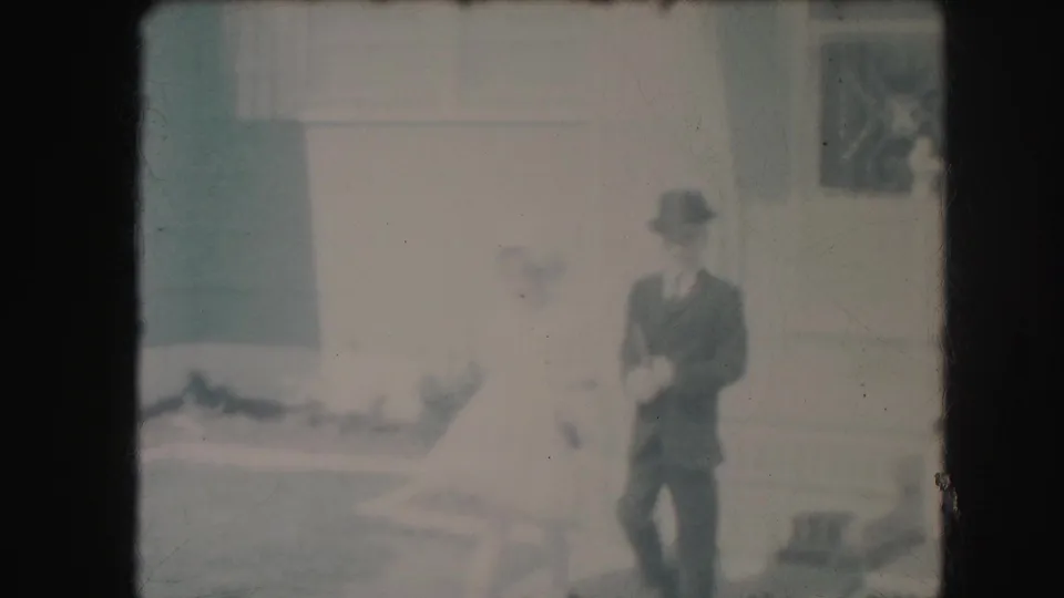 In 1959 Kansas City home-movie footage, a formally dressed boy stands near a girl in a white dress in a suburban yard.