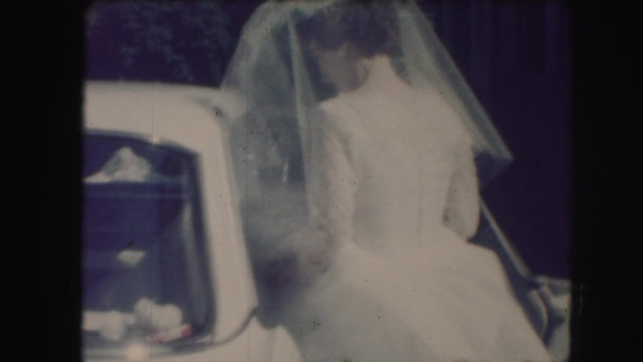 A veiled bride in a white wedding dress stands next to an open car door during the 1959 Kansas City wedding departure.