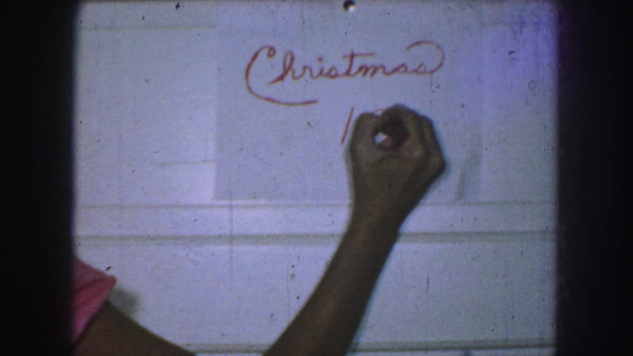 A hand writes below the word Christmas on a white wall.