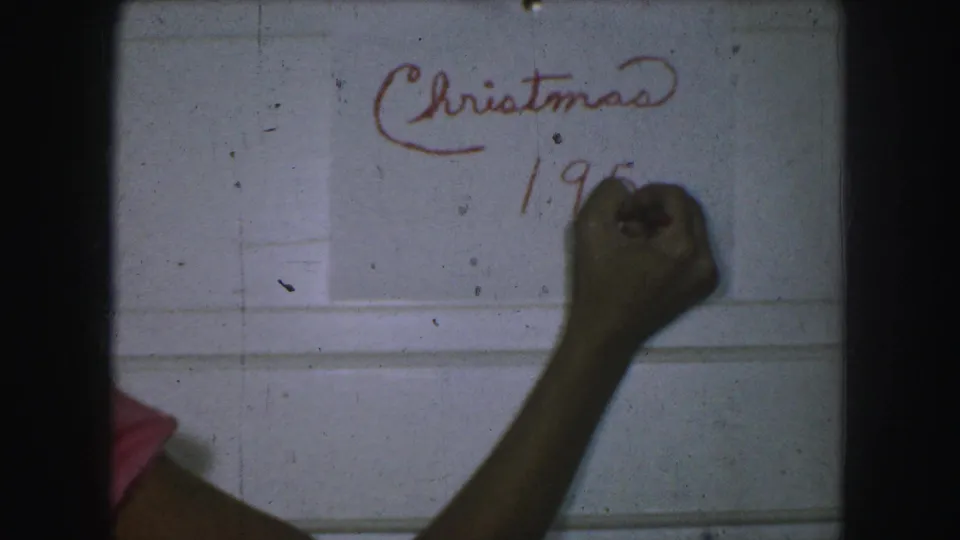 The red marker date is partly formed beneath Christmas as a hand writes on a white wall, with 8mm dust and gate shadow visible.