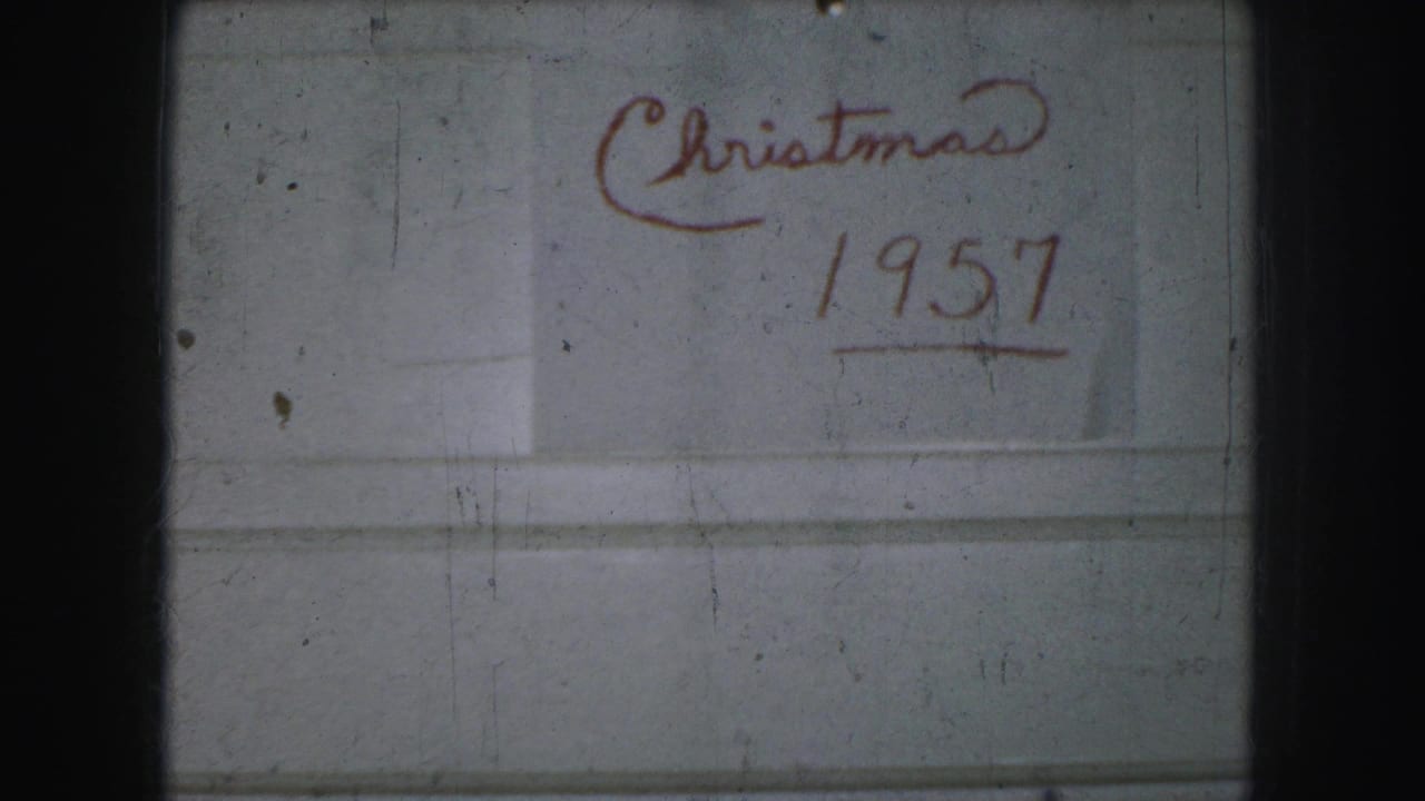Kansas City home-movie frame showing “Christmas 1957” handwritten in red on a pale surface, with visible 8mm frame edges and dust.