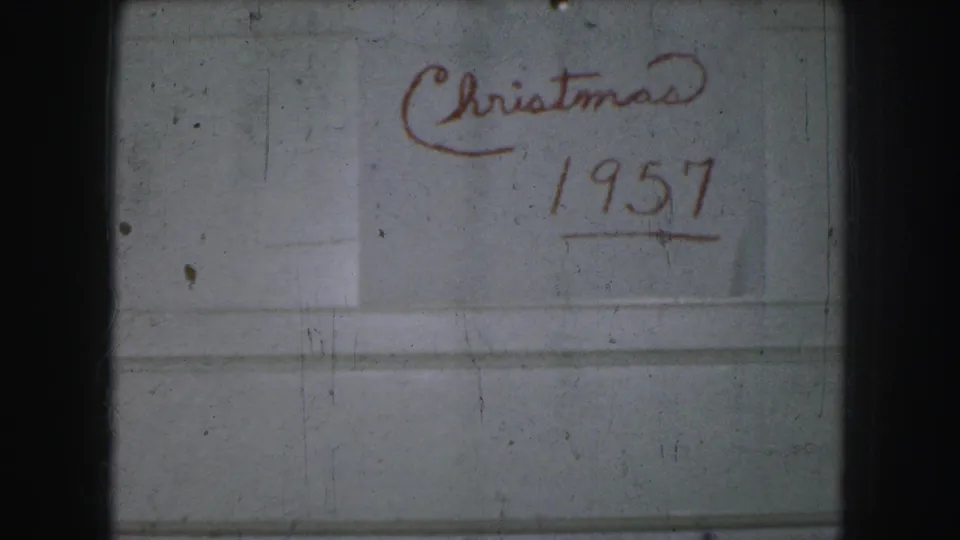 Kansas City home-movie frame showing “Christmas 1957” handwritten in red on a pale surface, with visible 8mm frame edges and dust.