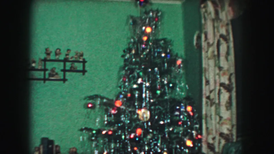 The final frame holds on the illuminated Christmas tree, with tinsel and ornaments visible beside patterned curtains in the Kansas City interior.