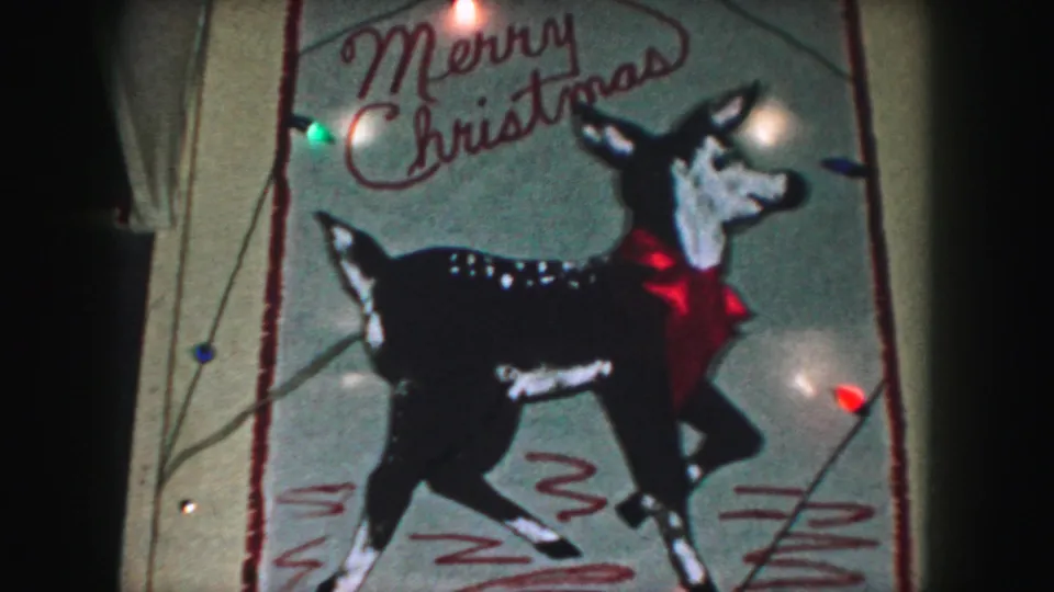 1959 Kansas City home-movie frame showing a painted reindeer, red bow, Merry Christmas text, and glowing holiday bulbs.