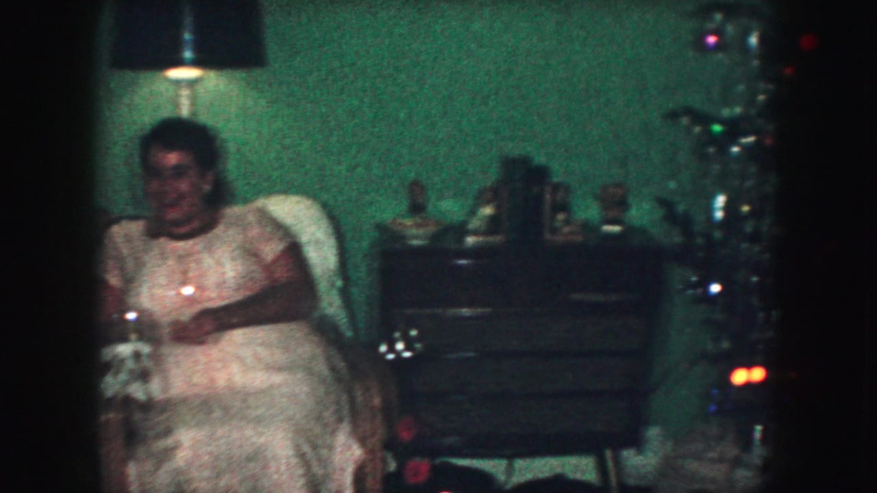 Woman seated in a living room beside a decorated Christmas tree and dresser.