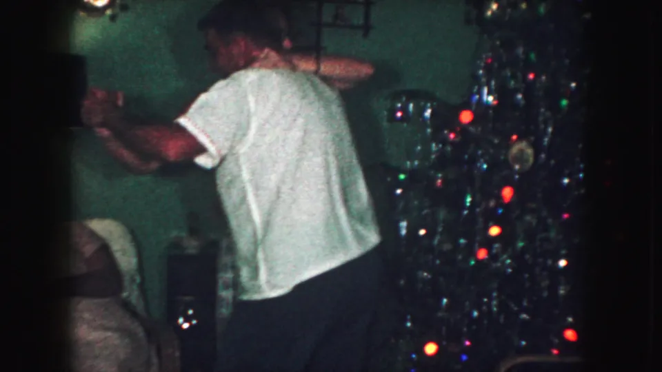A man in a white short-sleeved shirt moves beside the Christmas tree in the Kansas City living-room scene.