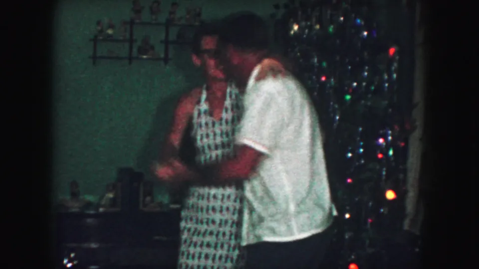 The adult couple continues dancing in the 1959 Kansas City living room, with colored Christmas lights and shelves visible behind them.