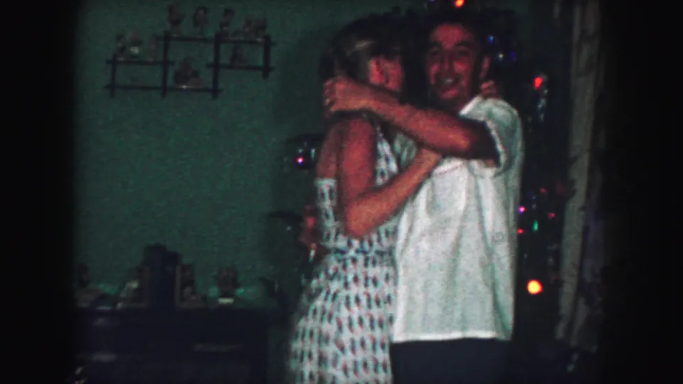 An adult man smiles toward the camera while embracing the woman during a Christmas dance in the Kansas City home interior.
