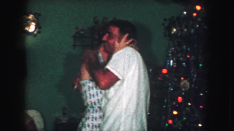 The couple kisses while holding each other beside the lit Christmas tree in this 1959 Kansas City home-movie frame.