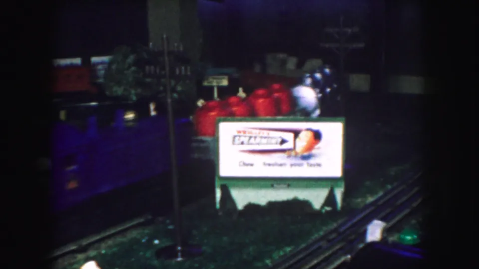 A model train passes through a 1959 Kansas City holiday display with red cars, tracks, and a visible Wrigley's Spearmint sign.