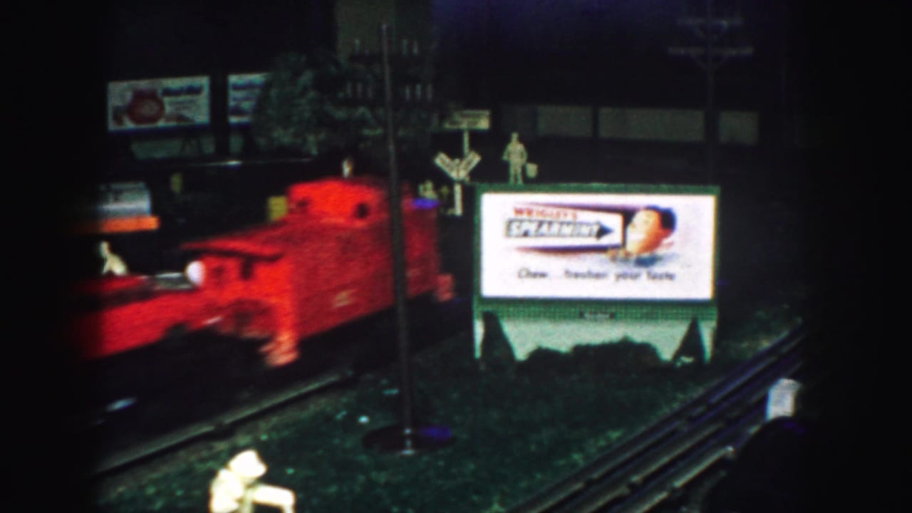 Red model train passes a Wrigley's Spearmint billboard on a miniature railroad layout.