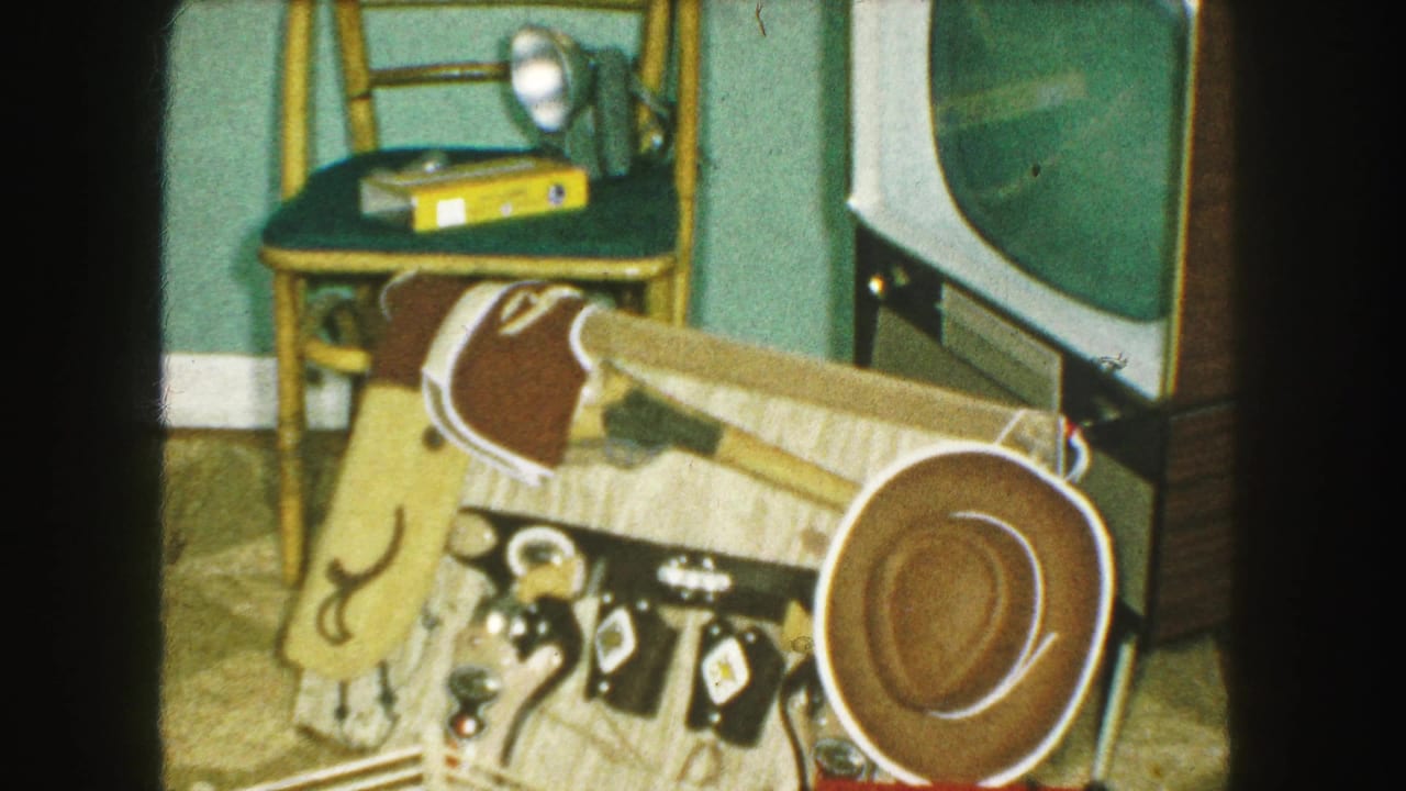 1959 Kansas City home-movie frame showing a toy cowboy hat, Western play accessories, and a television in a private domestic room.