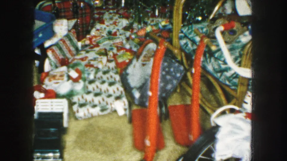 1959 Kansas City Christmas room with wrapped gifts, toys, a red tricycle, plaid chair, and household furniture.