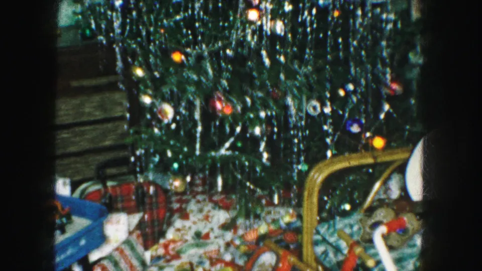 1959 Kansas City Christmas interior with a tinsel-covered tree, colored bulbs, presents, toys, and part of a tricycle.