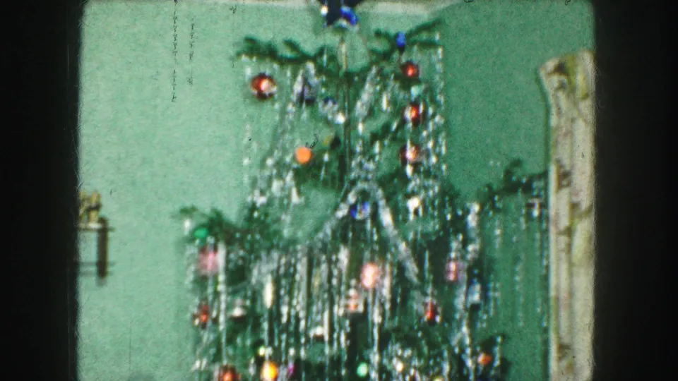 1959 Kansas City home interior frame showing the top half of a decorated Christmas tree with tinsel and multicolored ornaments.