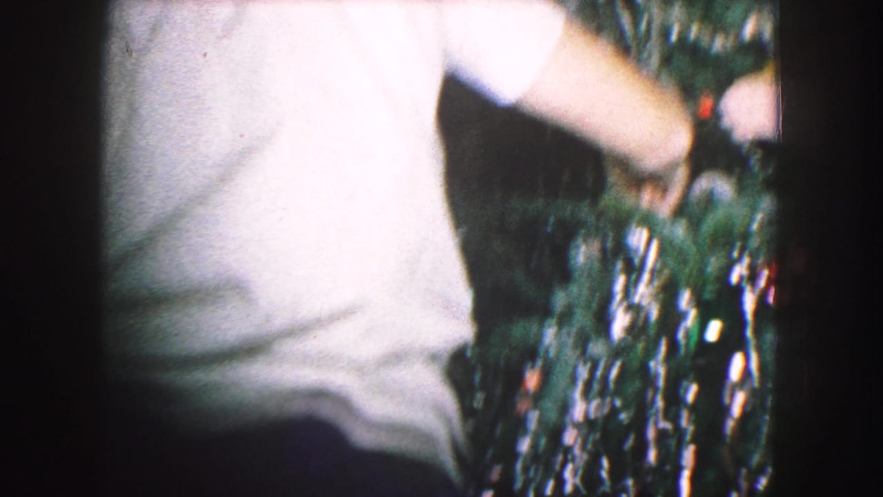 Person in a light shirt reaches toward a decorated Christmas tree with tinsel and lights.