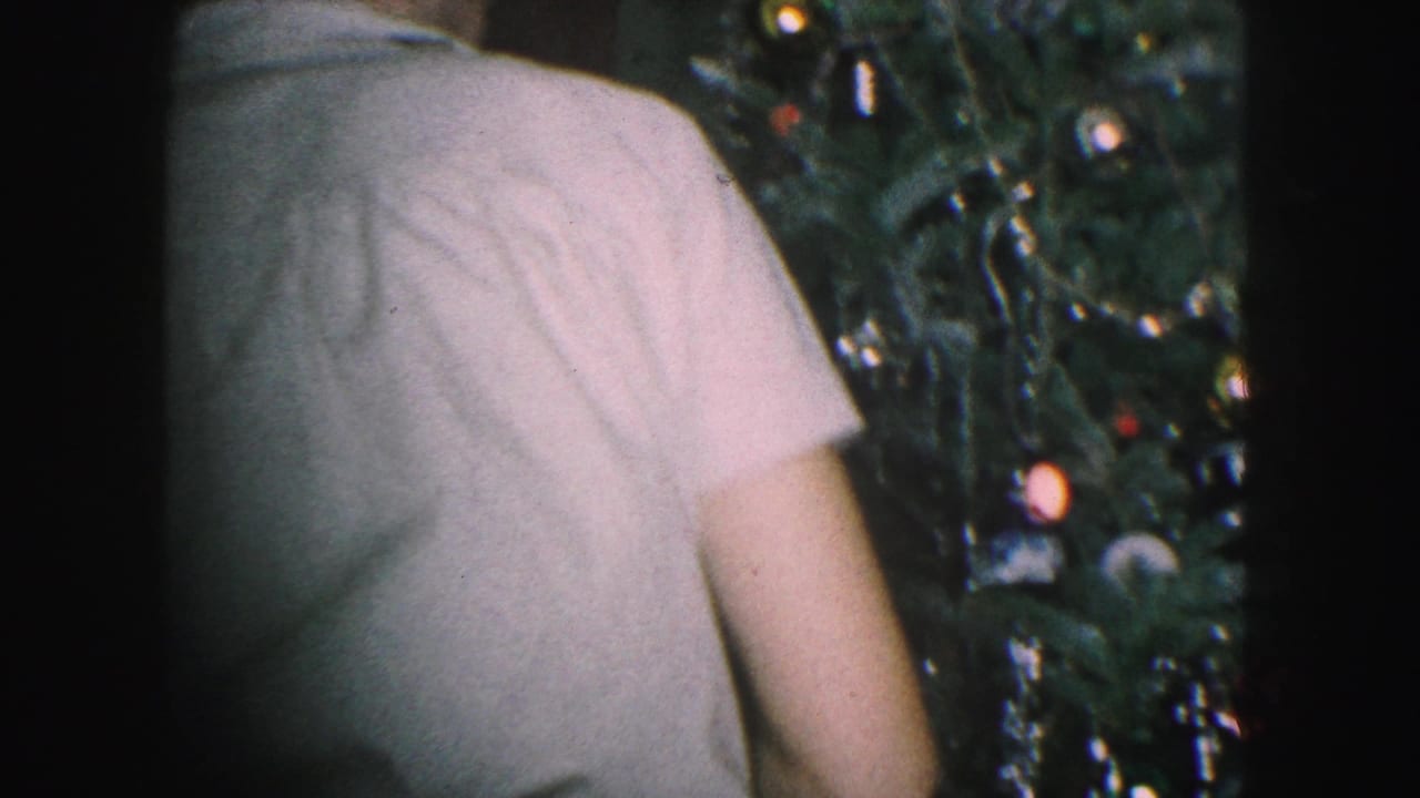 1959 Kansas City home-movie frame with a person seen from behind next to a decorated Christmas tree in a dim room.