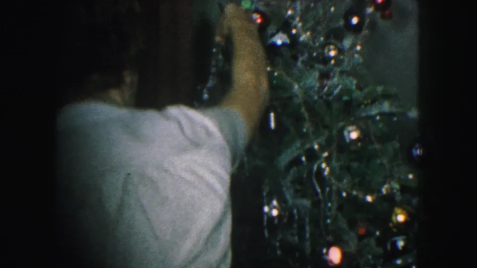 Close 1959 home-movie view of a person adjusting decorations on a Christmas tree in a Kansas City interior.
